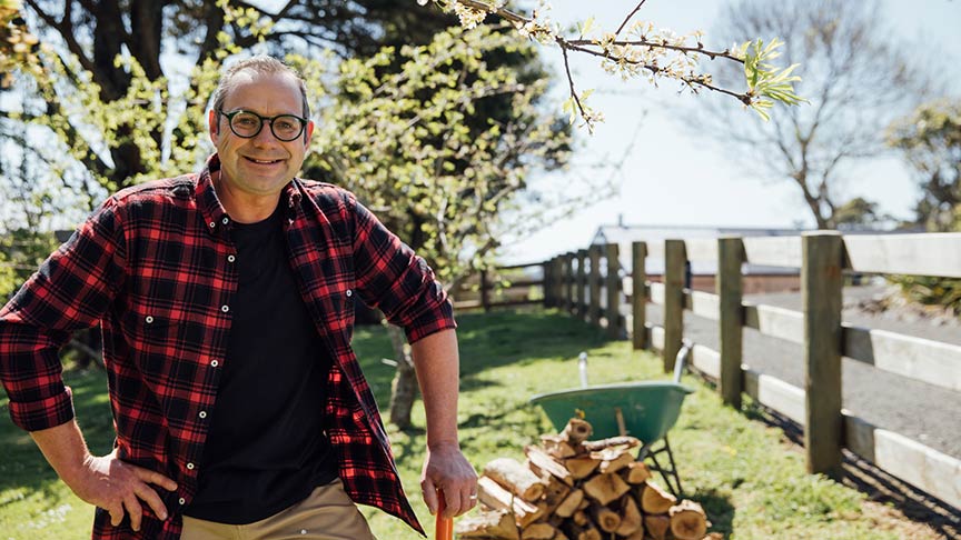 Michael van de Elzen standing in front of chopped wood and wheelbarrow 