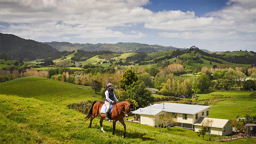 woman riding horse on hill with house in background 