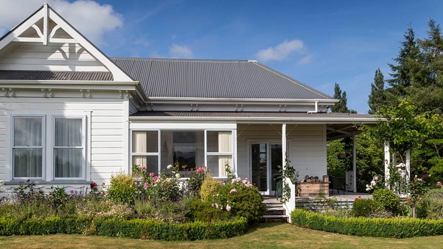 white weatherboard villa with grey roof and landscaped garden in front 