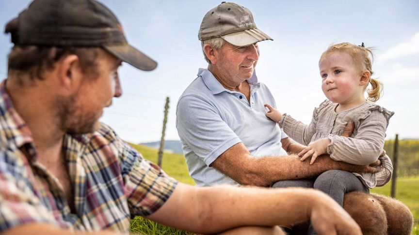 Two men sitting next to each other with young girl sitting on older man's lap 