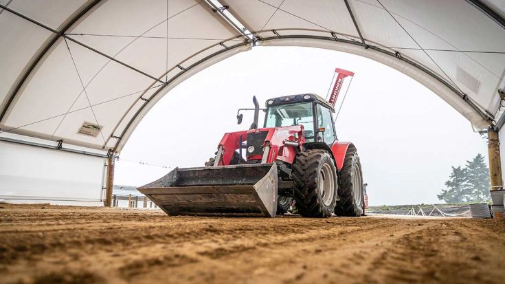 Red tractor inside large white domed shed 