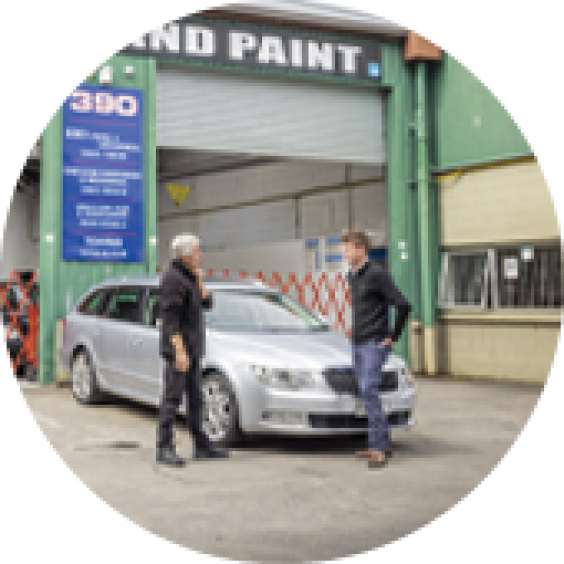 two men talking in front of car parked in a dealership 