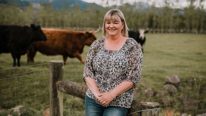 Vicky Phillips leaning against fencepost with cows in back paddock
