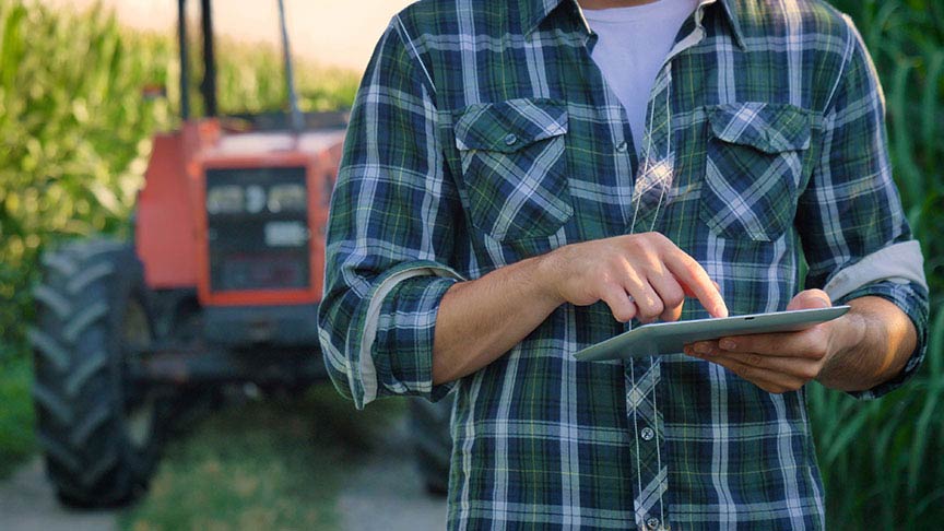 farmer using a tablet standing in front of red tractor 