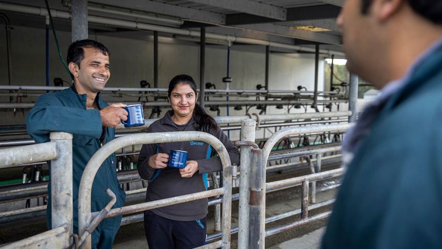 Man and woman with mugs talk over metal fence to another man 