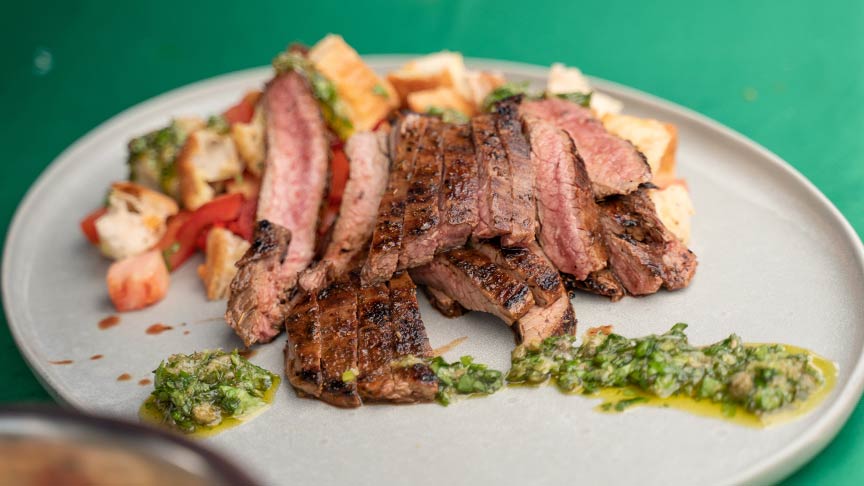 plate of cut steak with green sauce next to meat. 