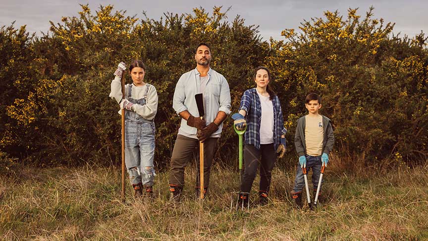 family of four standing in garden holding farming tools 