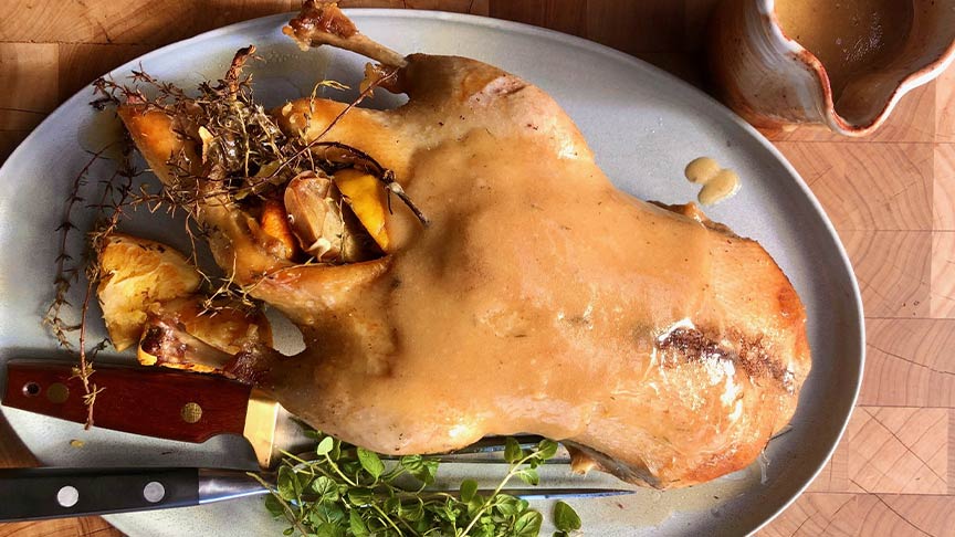 Roast duck with herbs on plate next to carving tools 