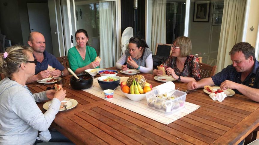 group of six people eating around wooden outdoor table with fruit bowl in the middle 