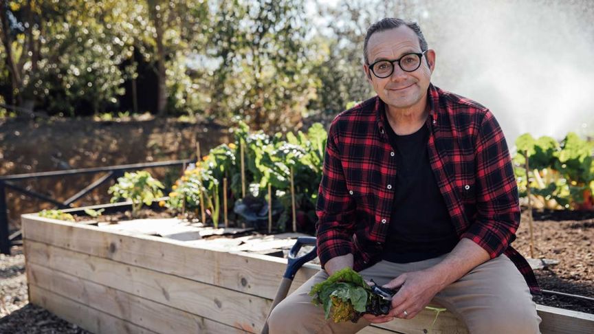 Michael van de Elzen sitting on garden planter box holding greens 