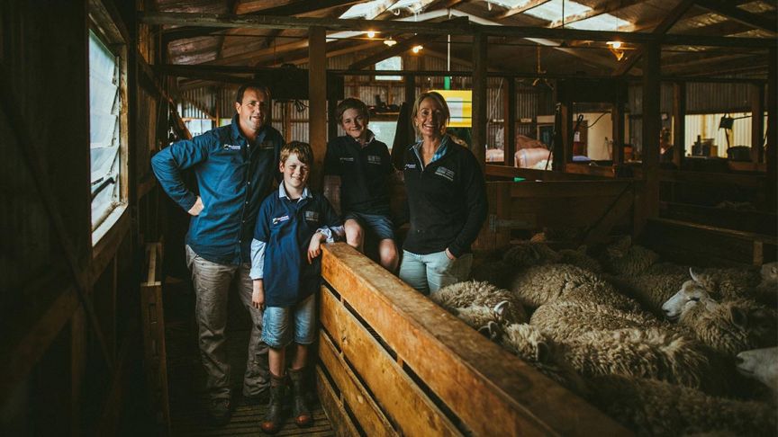 family of four standing in woolshed next to sheep pen 